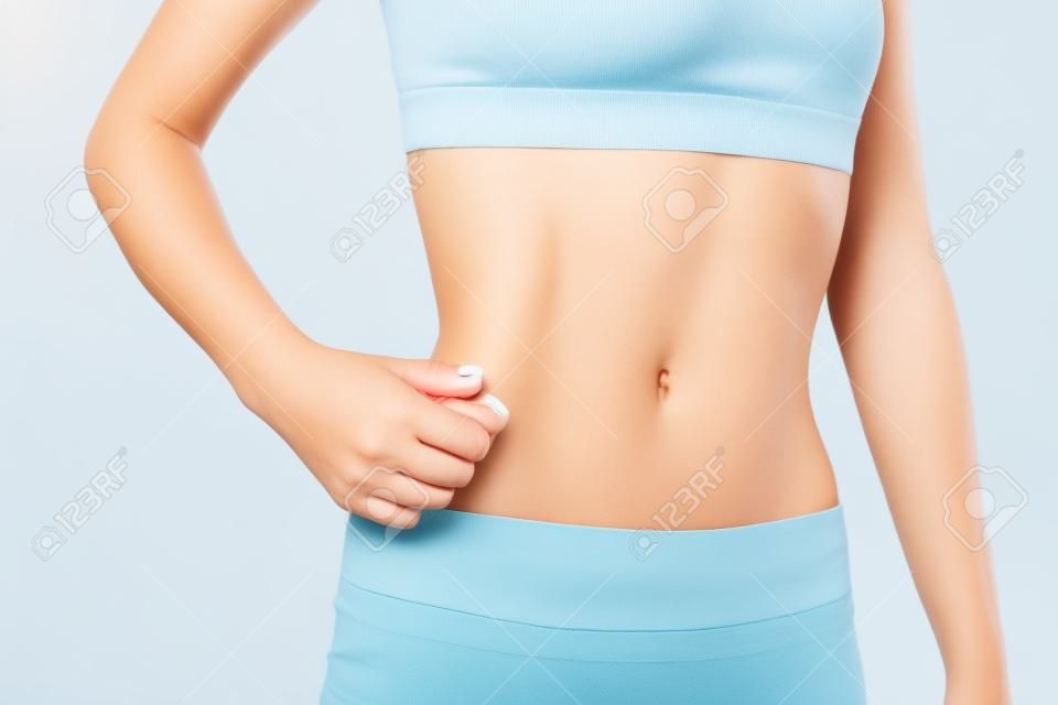Slim jovem mulher beliscar gordura em sua barriga, fitness e conceito de perda de peso
