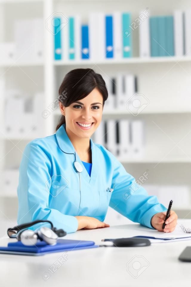 Médico feminino que trabalha na mesa do escritório, ela está sorrindo para a câmera, profissionais de saúde