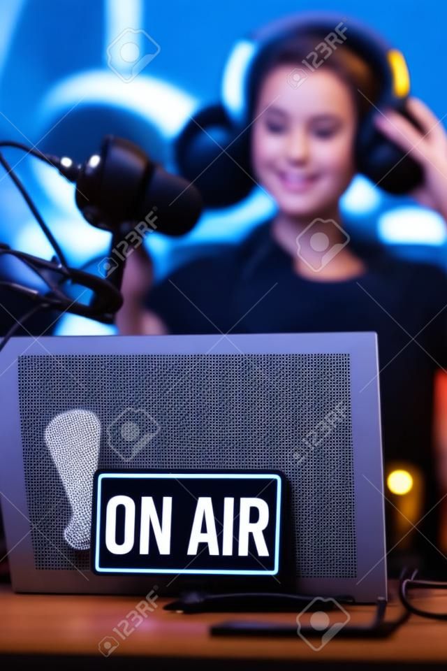 Giovane conduttore radiofonico che si prepara per la trasmissione, indossa le cuffie, in primo piano il cartello in onda