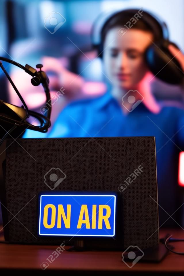 Young radio host getting ready for broadcasting, she is wearing headphones, on air sign in the foreground