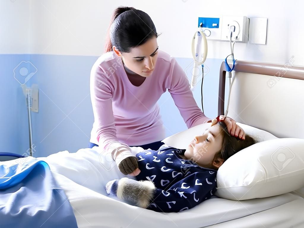 Jovem mulher confortando seu filho doente deitado na cama no hospital, ela está tocando sua cabeça, pediatria e conceito de saúde