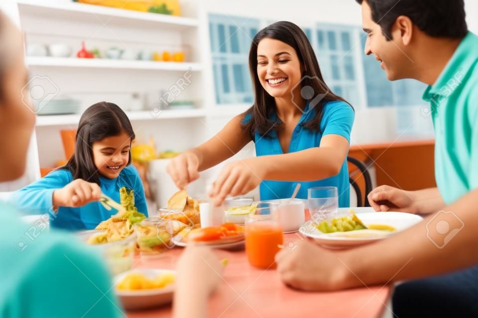 Familia hispana sentado en la mesa comiendo comida junto