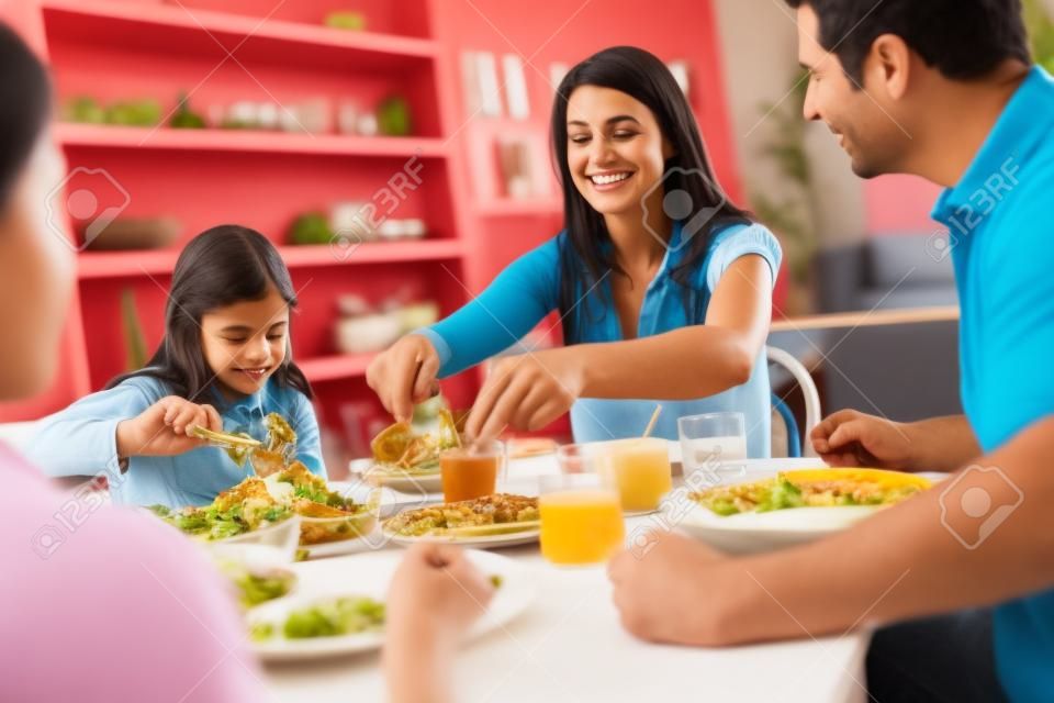 Familia hispana sentado en la mesa comiendo comida junto