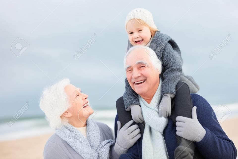 祖父母と孫娘の冬の浜辺を歩く