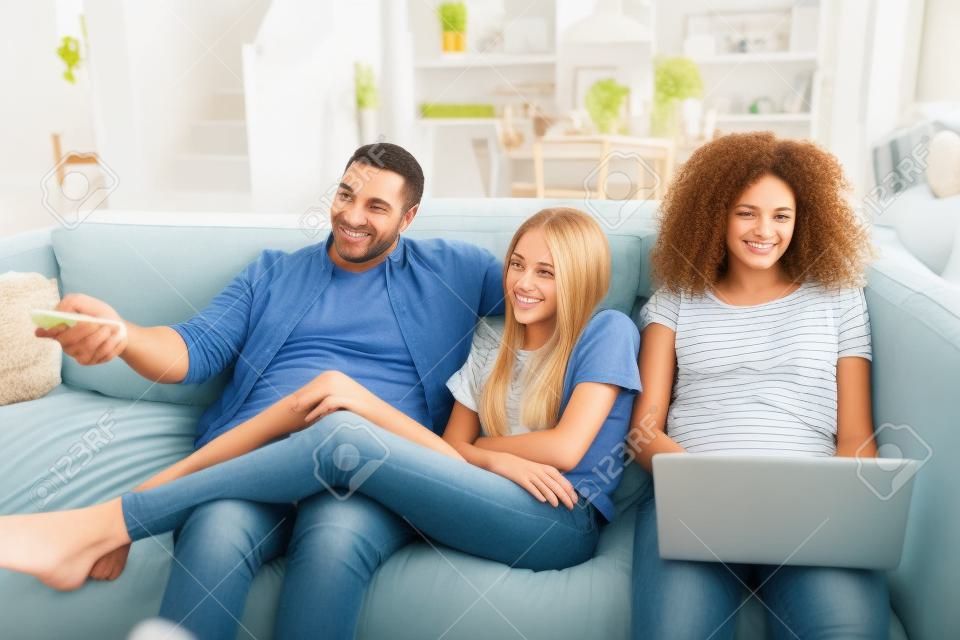 Отец сидит на диване и смотрит телевизор с дочерьми-подростками