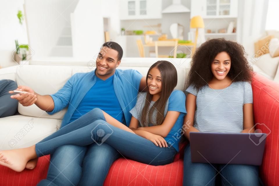 Отец сидит на диване и смотрит телевизор с дочерьми-подростками