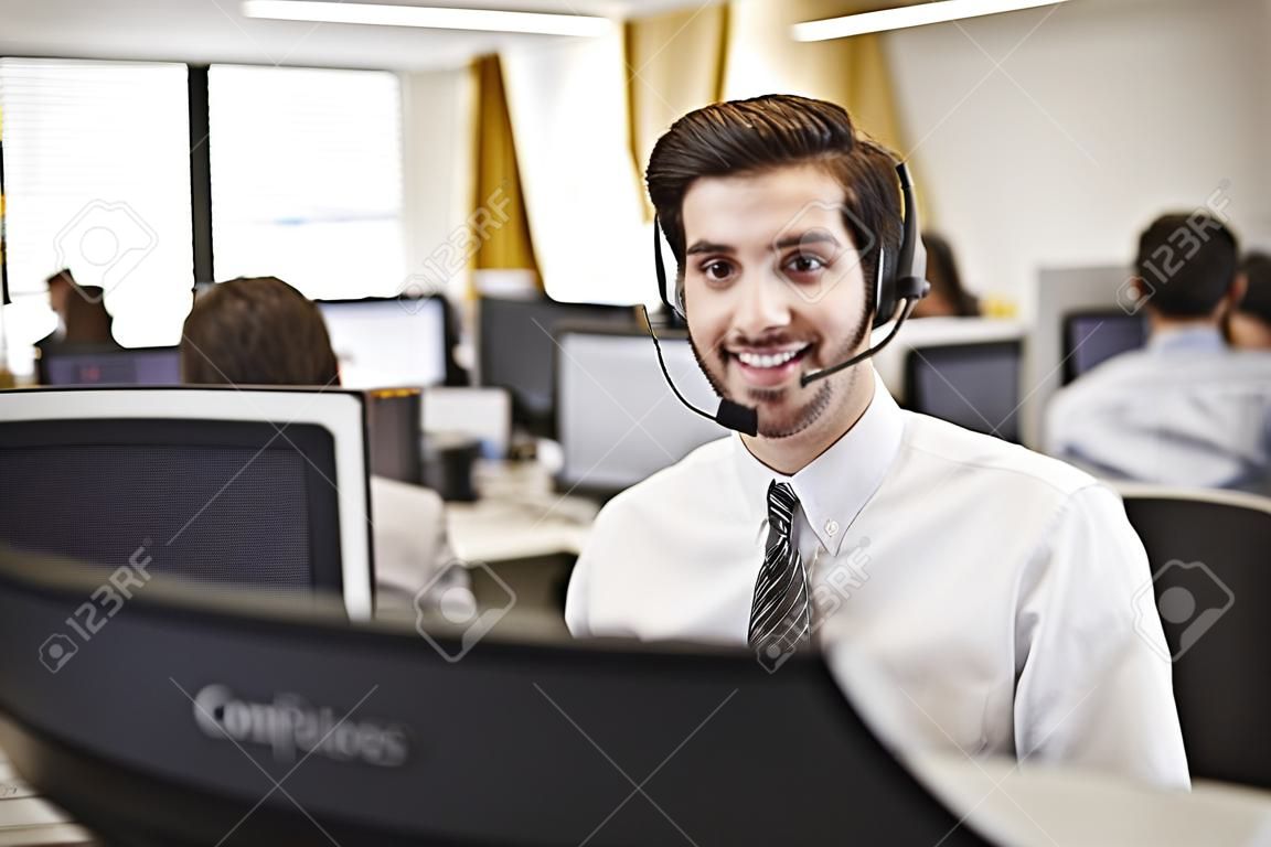 Jeune homme travaillant à l'ordinateur avec un casque dans le bureau occupé