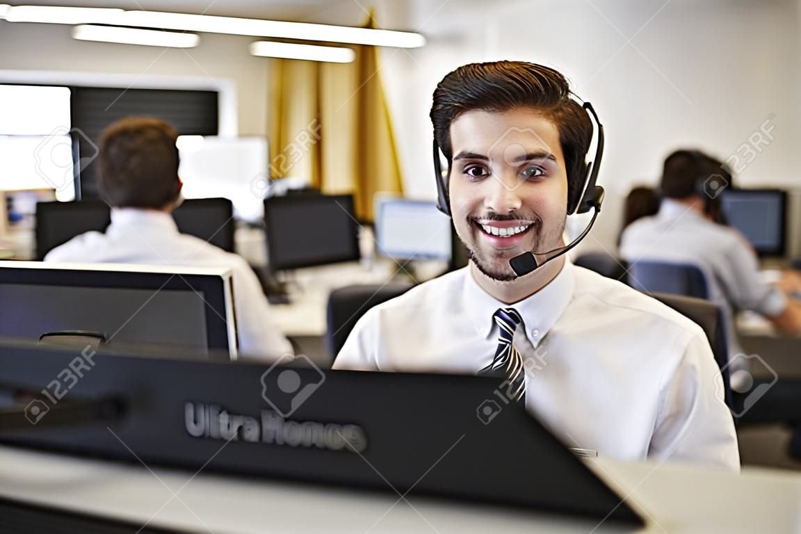 Jongeman die werkt op computer met headset in drukke kantoor
