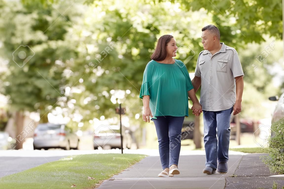 Senior pareja caminando por la calle suburbana cogidos de la mano