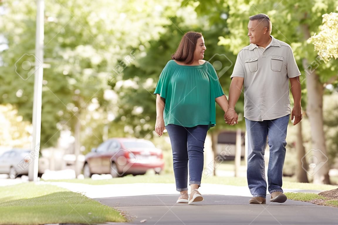 Senior pareja caminando por la calle suburbana cogidos de la mano