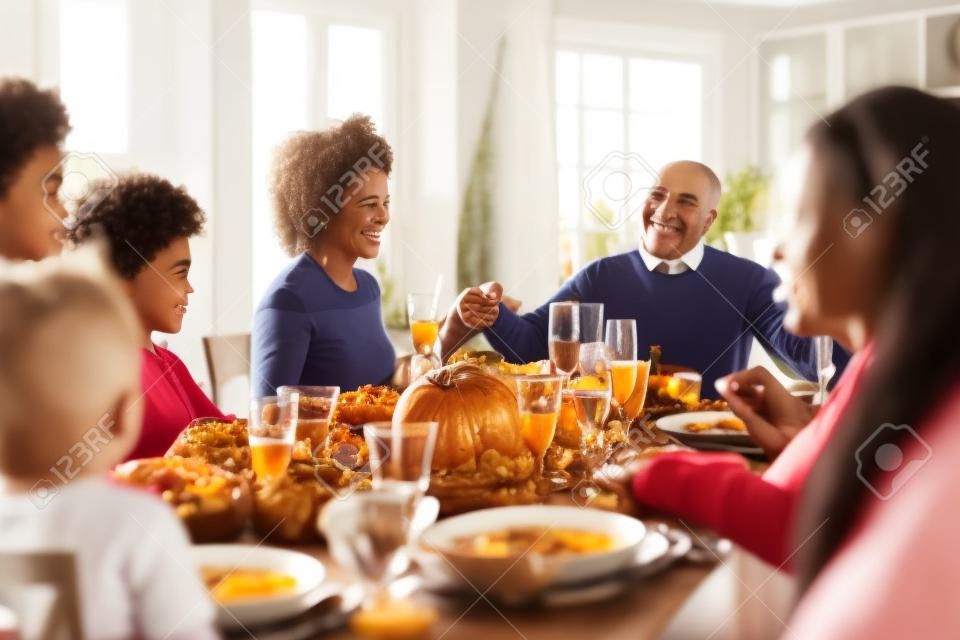 Famille mixte de plusieurs générations se tenant la main et disant grâce avant de manger à leur table de dîner de Thanksgiving, mise au point sélective