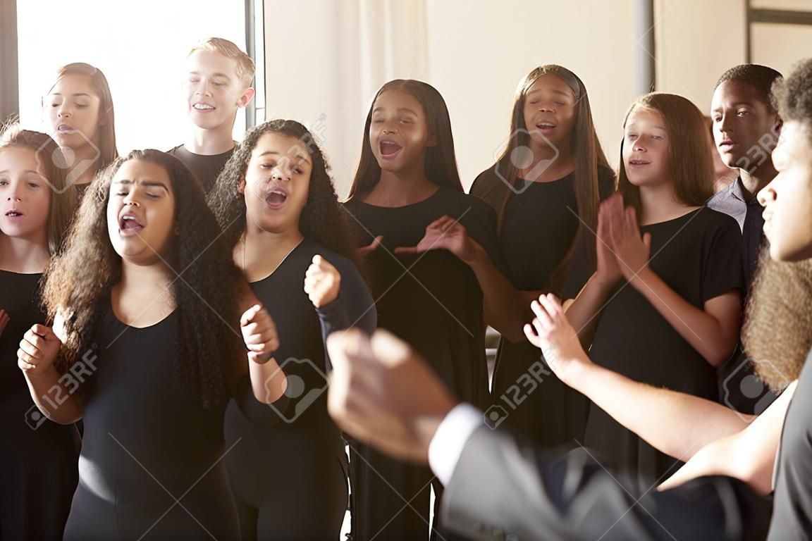 Estudiantes masculinos y femeninos cantando en coro con el maestro en la escuela de artes escénicas