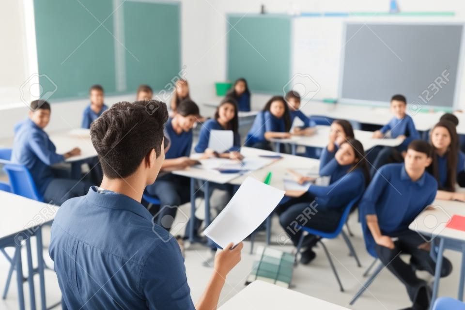 Rear View Of Male High School Teacher Standing At Front Of Class Teaching Lesson