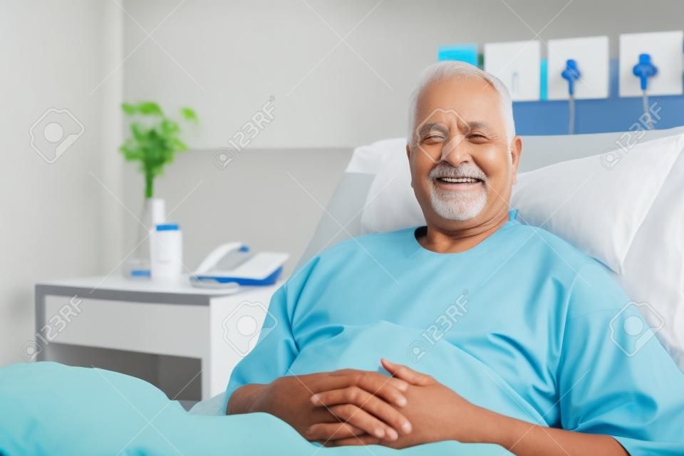 Portrait Of Male Senior Patient Lying In Hospital Bed Smiling At Camera