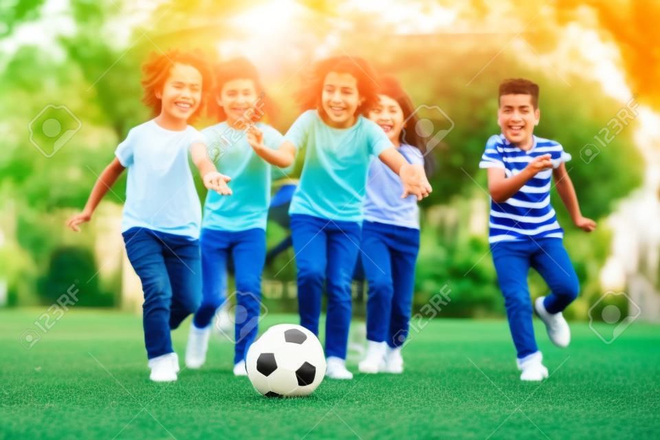 Grupa dzieci grających w piłkę nożną z przyjaciółmi w parku