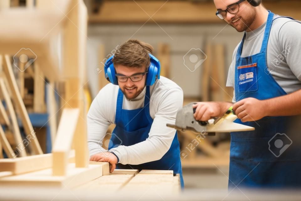 Tutor mit männlichem Zimmermannsschüler in der Werkstatt, der für die Ausbildung am College mit Tischsäge studiert