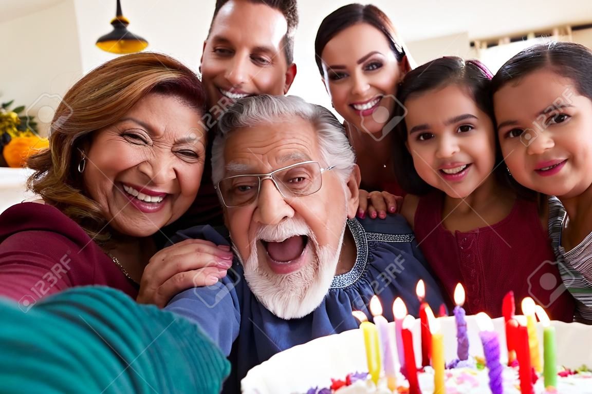 Une famille hispanique multigénérationnelle prend un selfie pour célébrer l'anniversaire de sa petite-fille à la maison