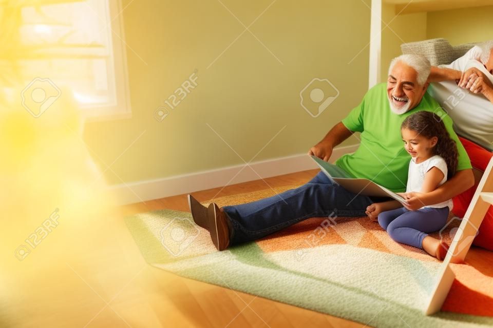 Abuelo y nieta hispanos sentados en el piso del dormitorio de los niños leyendo un libro juntos