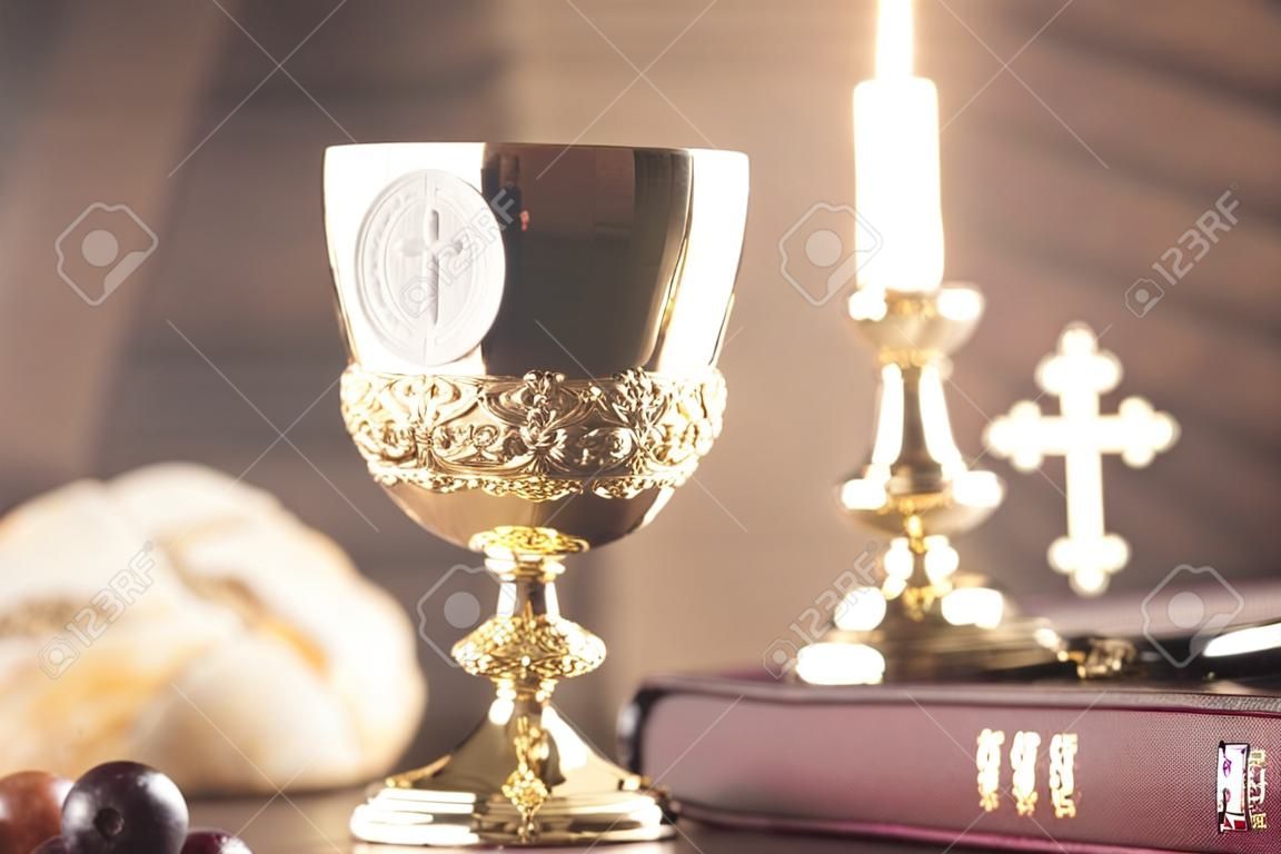 Tema da religião católica. Bíblia Sagrada, a cruz e o cálice de ouro na mesa de pedra e no fundo de pedra.