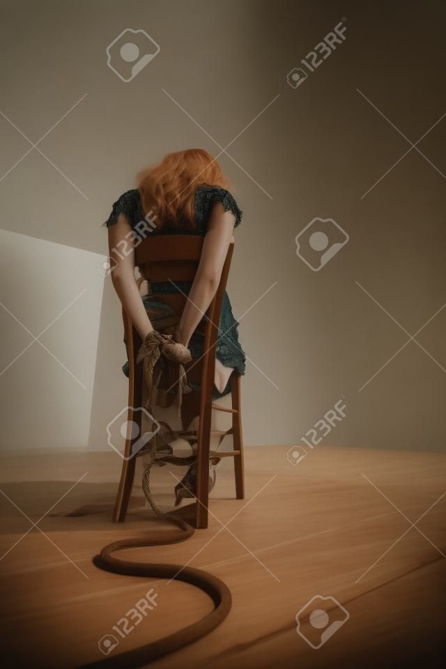 Mujer joven atada a una silla en una habitación vacía