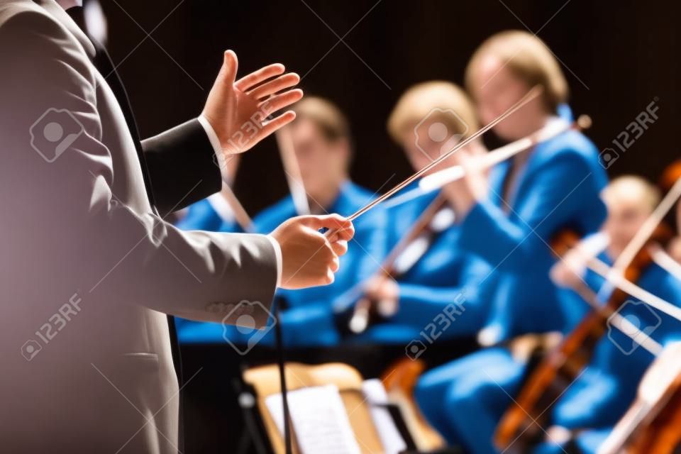 Conductor dirigir la orquesta sinfónica con artistas en el fondo, con las manos en primer plano.