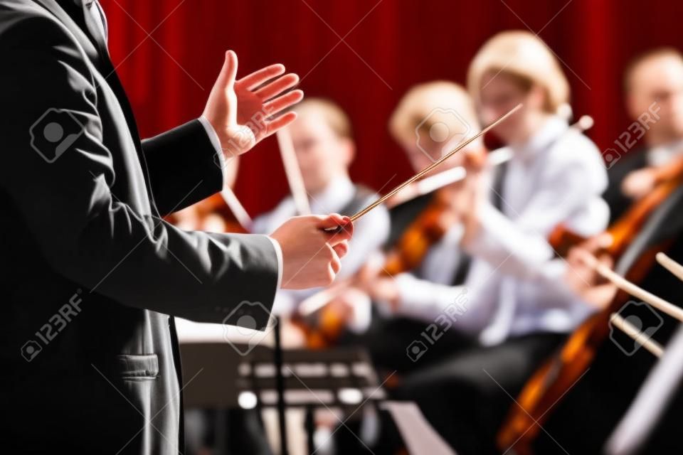 Direttore d'orchestra dirigere un'orchestra sinfonica con artisti sullo sfondo, le mani close-up.