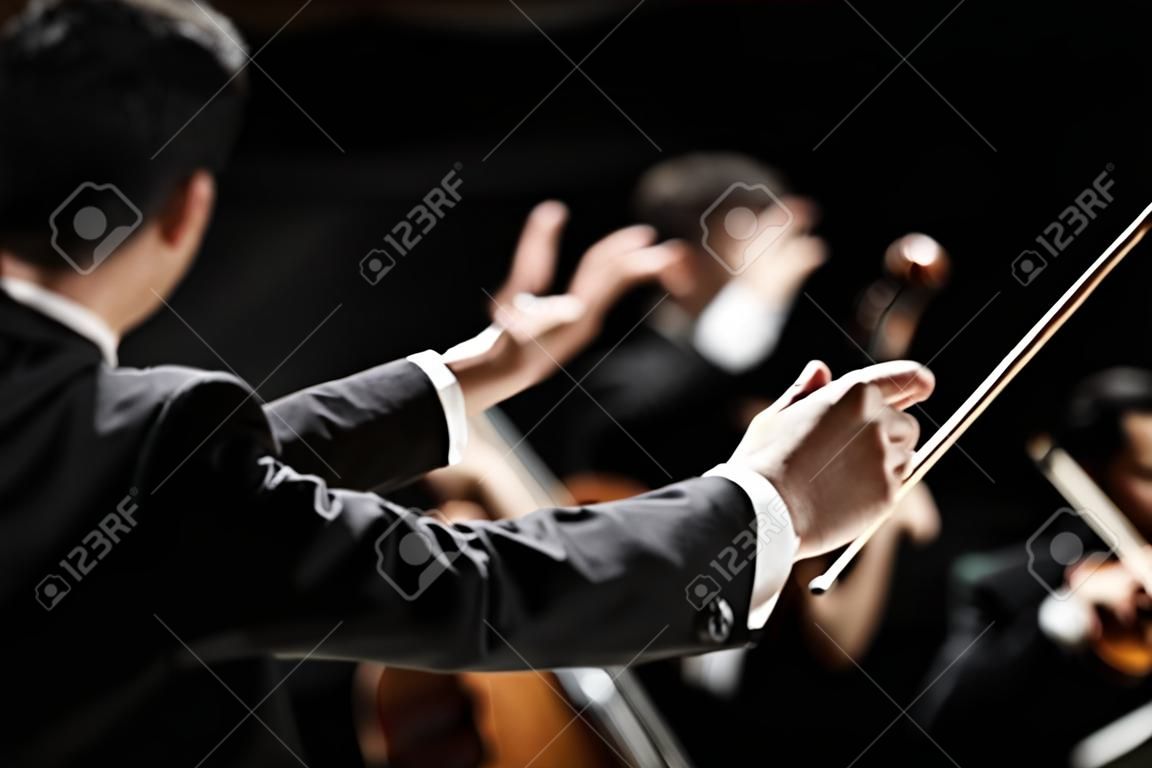 Direttore dirigere orchestra sinfonica con artisti sullo sfondo, mani close-up.