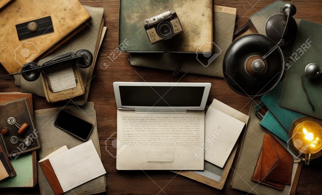 Messy vintage desktop with laptop, phone, lamp, camera and folders, top view