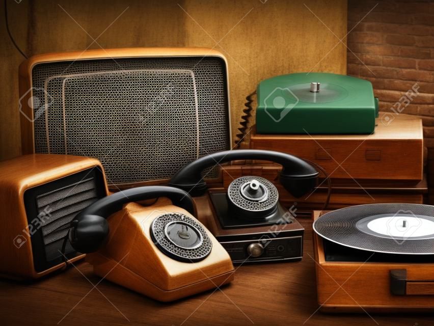 ヴィンテージレトロなリバイバルオブジェクトと中古の家電製品のコレクションをテーブルの上に:レコードプレーヤー、テレビ、ラジオ、ロータリーダイヤル電話