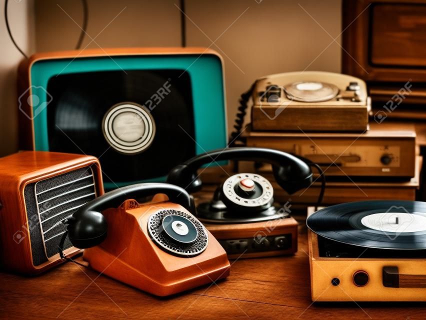 ヴィンテージレトロなリバイバルオブジェクトと中古の家電製品のコレクションをテーブルの上に:レコードプレーヤー、テレビ、ラジオ、ロータリーダイヤル電話