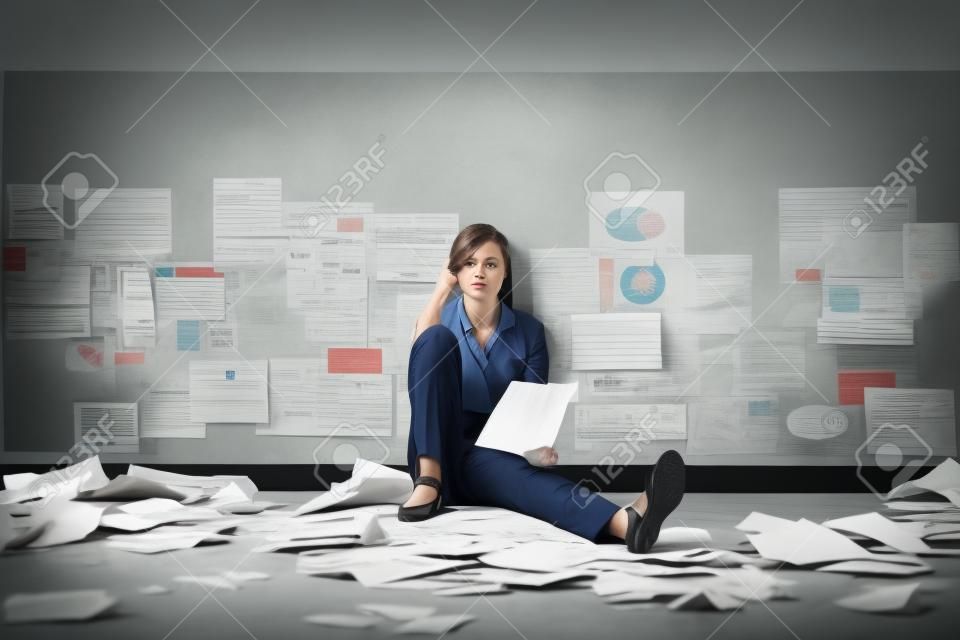 Wanhopige gestresste zakenvrouw die op de vloer zit omringd door verkruimeld papierwerk: business failure and crisis concept