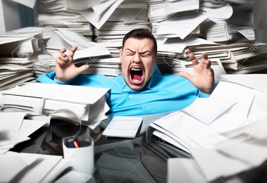 Krzyczący biznesmen tonący pod mnóstwem papierkowej roboty w biurze, jest przytłoczony pracą i szaleje