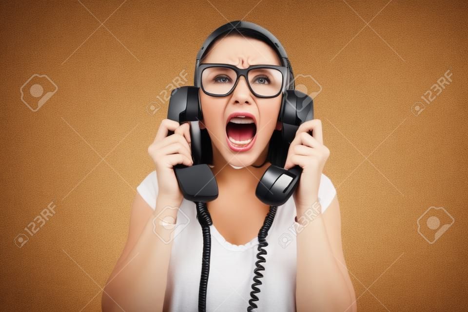 Mujer sosteniendo dos receptores de teléfono y gritando, está estresada y enojada