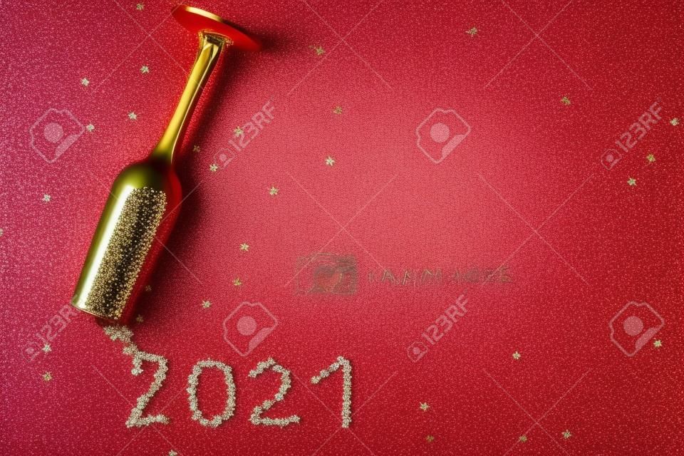 Bicchiere da champagne con paillettes a forma di stella sparse a forma di iscrizione 2021 su fondo rosso. Festa, Capodanno, concetto di celebrazione. Vista dall'alto. Disposizione piatta.