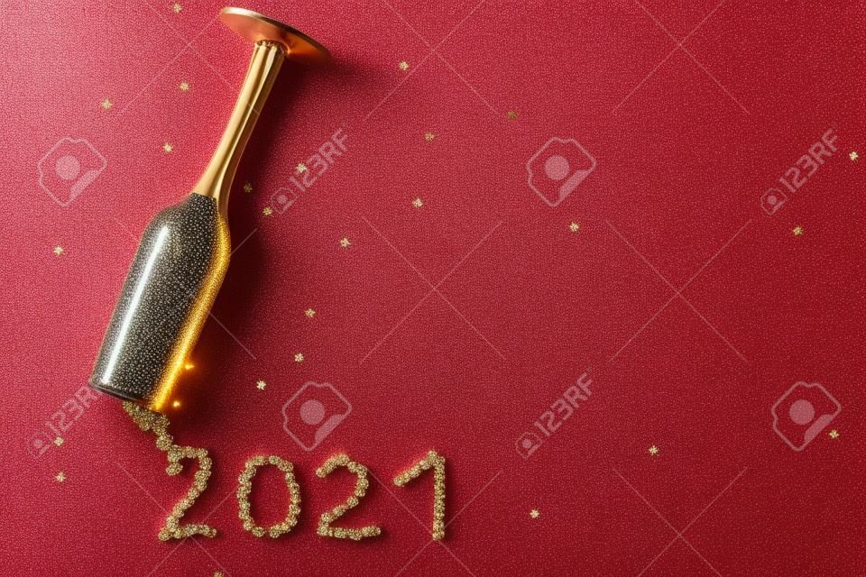 Champagnerglas mit sternförmigen Pailletten, die in Form der Aufschrift 2021 auf rotem Grund verstreut sind. Party, neues Jahr, Feierkonzept. Ansicht von oben. Flach liegen.