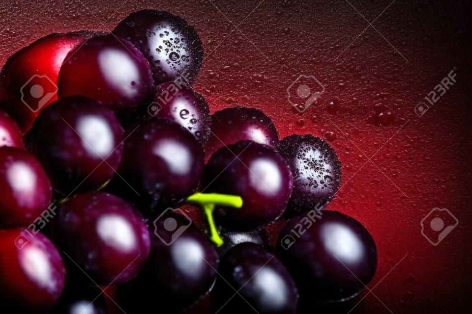 Primo piano di uve rosse fresche e scure con spruzzi d'acqua su sfondo scuro