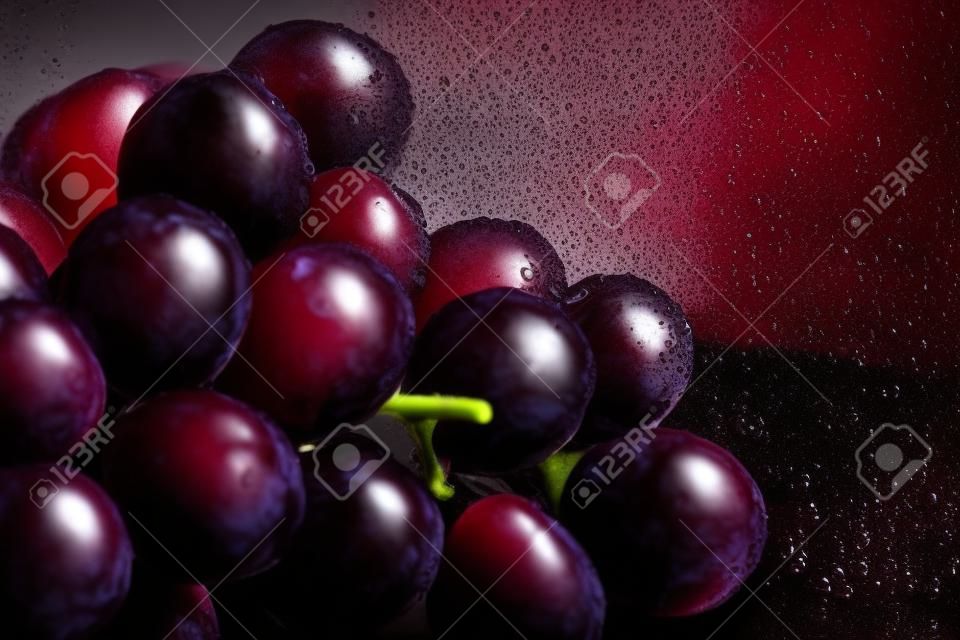 Primo piano di uve rosse fresche e scure con spruzzi d'acqua su sfondo scuro