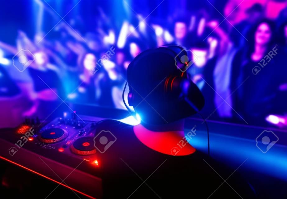 DJ met koptelefoon en dj set op avond club feest. Mensen op het feest hebben plezier op de achtergrond