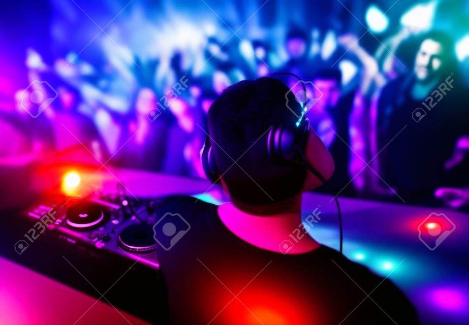 DJ met koptelefoon en dj set op avond club feest. Mensen op het feest hebben plezier op de achtergrond