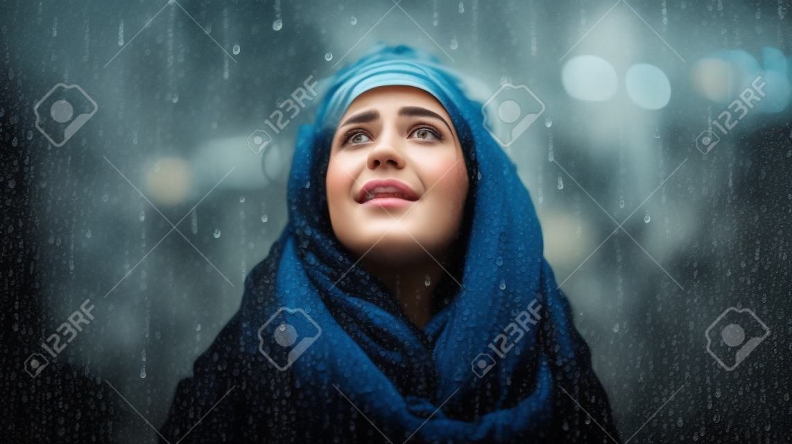 Portrait of a beautiful young woman with scarf in the rain.