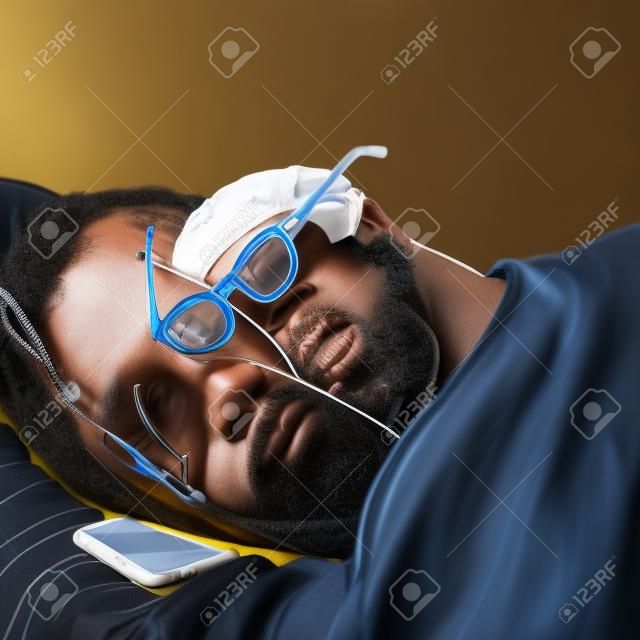 Um homem negro está dormindo com óculos, um telefone está deitado ao lado dele.