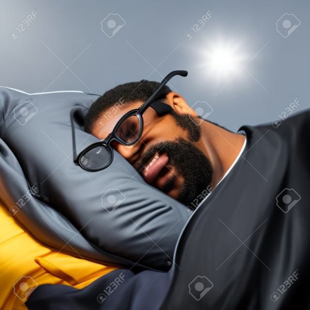 Um homem negro está dormindo com óculos, um telefone está deitado ao lado dele.