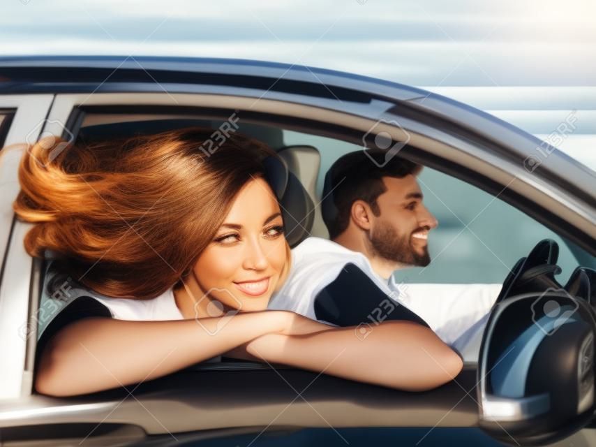 Kobieta wygląda przez okno samochodu, jej włosy powiewają na wietrze. mąż jeździ