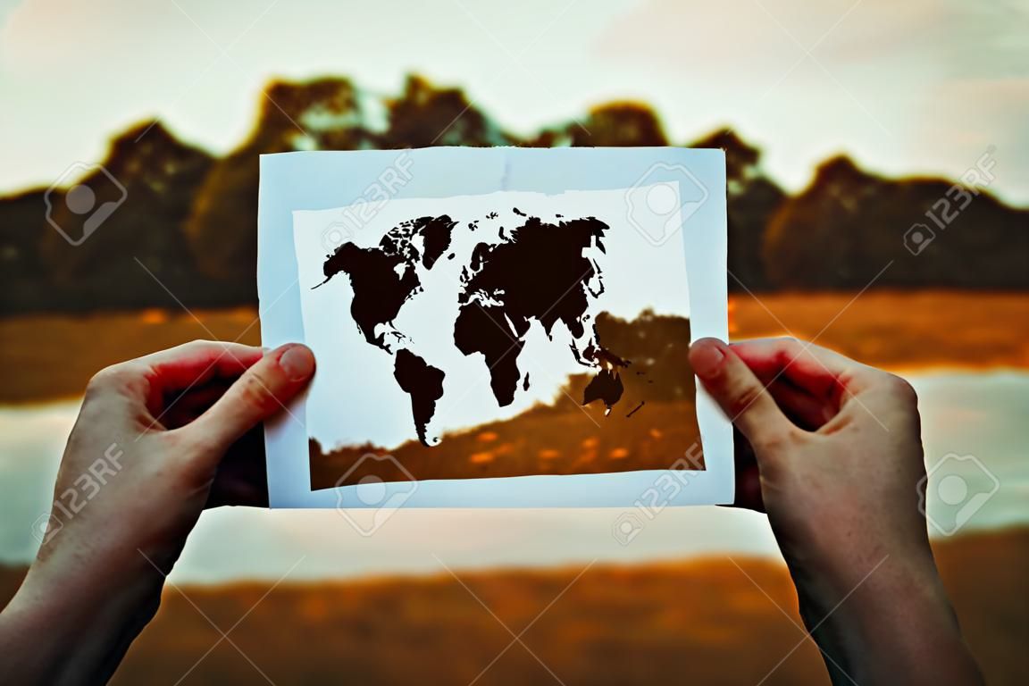 Climate change problem, destruction of nature concept. Human hands holding a paper sheet with world map icon over a dry grass field background. Global warming, solar radiation and pollution risk.