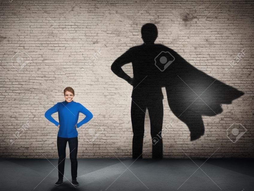 Casual teenage, keeps arms on hips smiling confident, casting a superhero with cape shadow on the wall. Student ambition success concept. Leadership hero power, motivation and inner strength symbol.