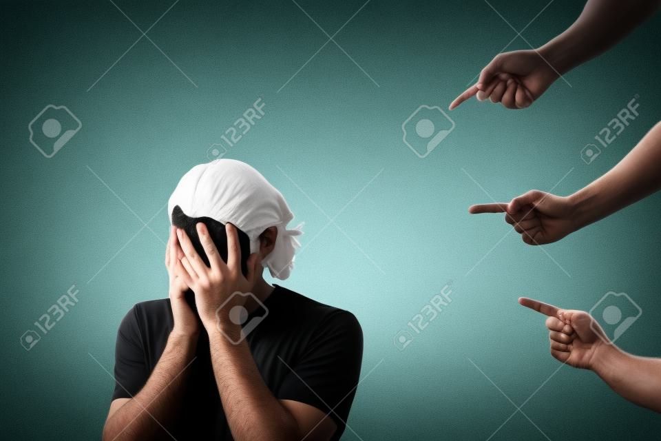 Disappointed and ashamed man, covers his face with palms, as many people fingers points to him from behind, blaming and scolding. Guy suffering emotional breakdown and depression, being under pressure