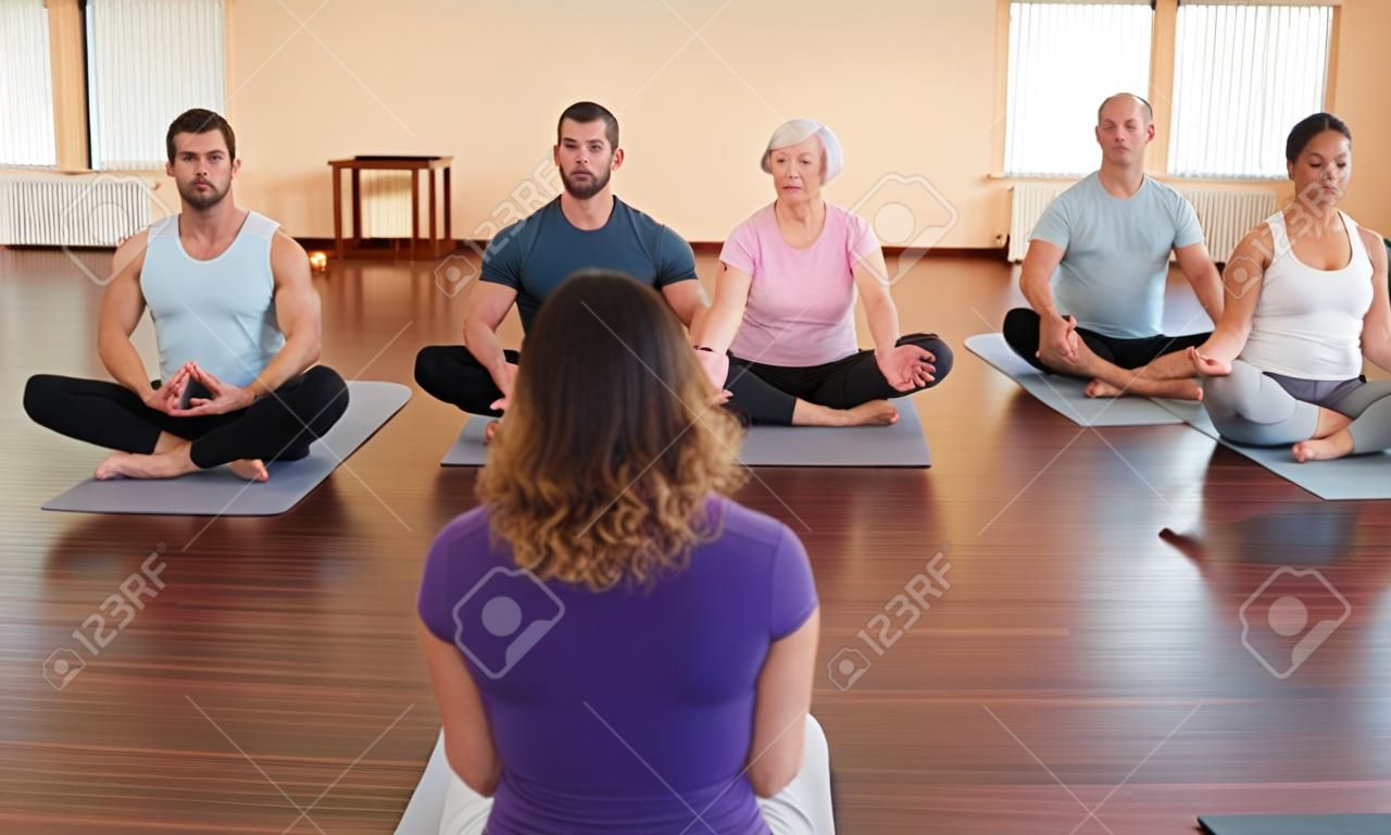 Fitness coach giving group yoga instructions in a gym