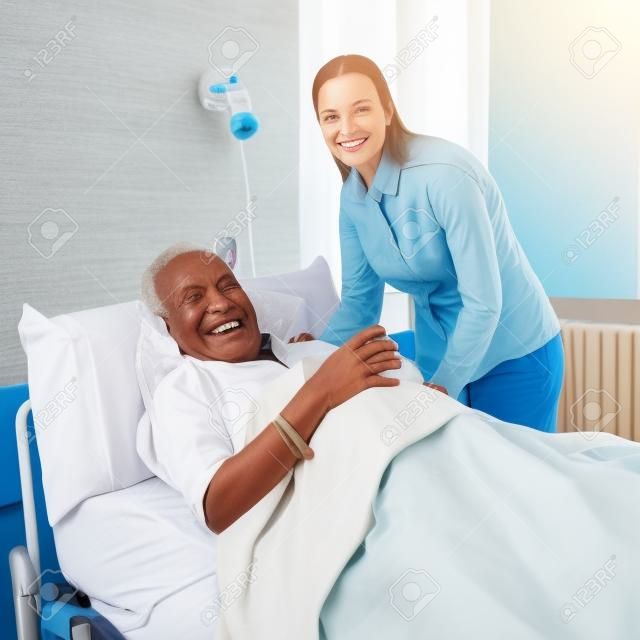 Mujer sonriente visitar hombre postrado en cama vieja en una cama de hospital