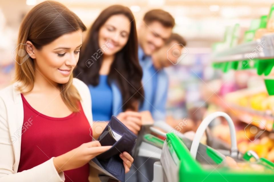 Zawstydzony kobieta szuka pieniędzy w swoim portfelu w kasie w supermarkecie