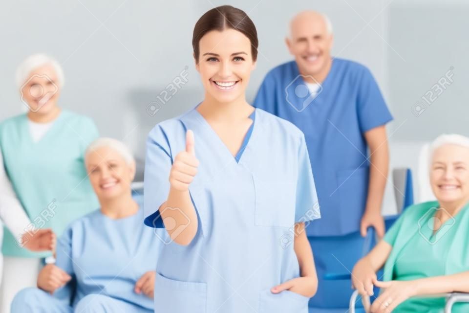 Happy nursing assistant holding her thumbs up in front of a happy group of senior people